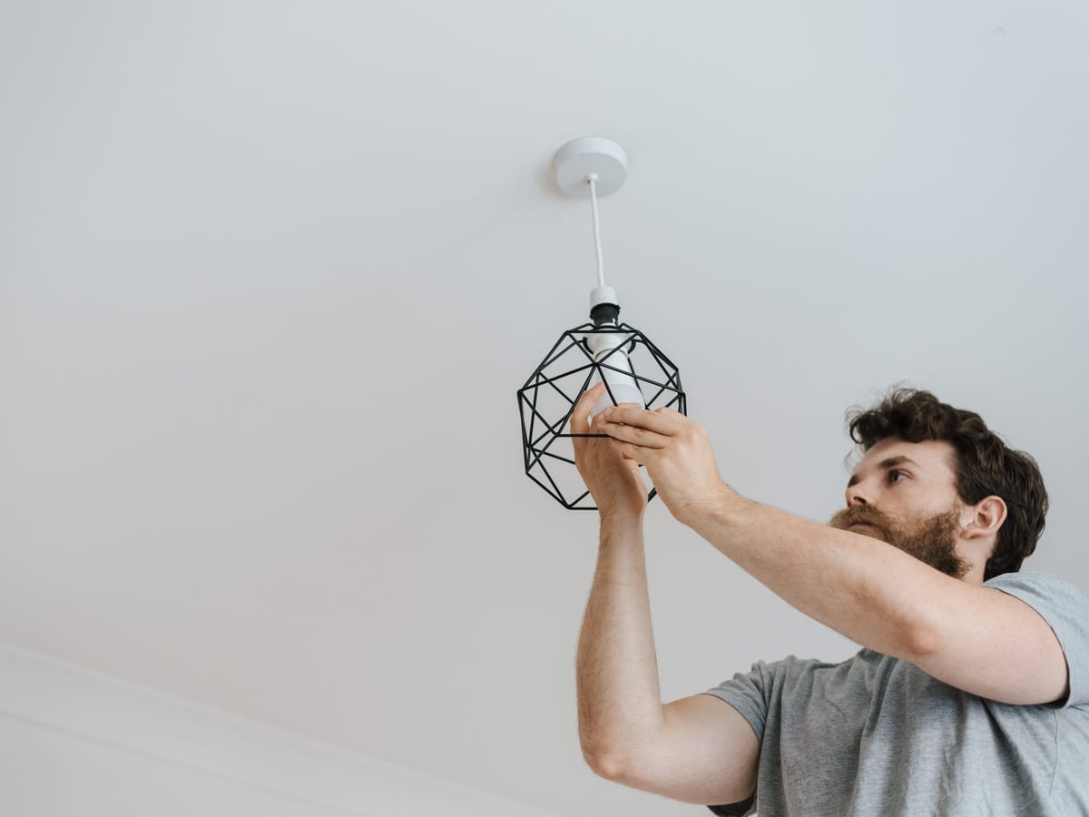 From below of male screwing light bulb into new fashionable lamp during renovation work in apartment.