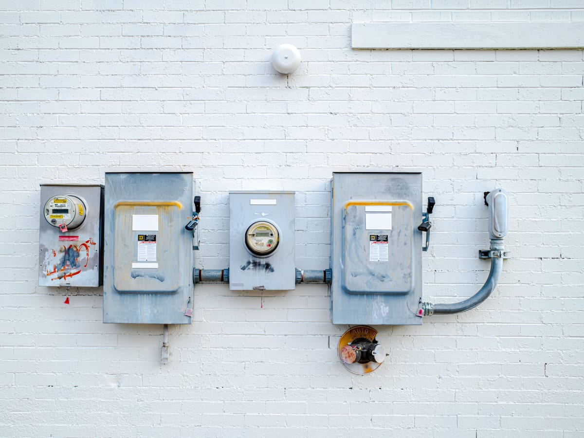Electrical boxes and power meters mounted on a white brick wall.
